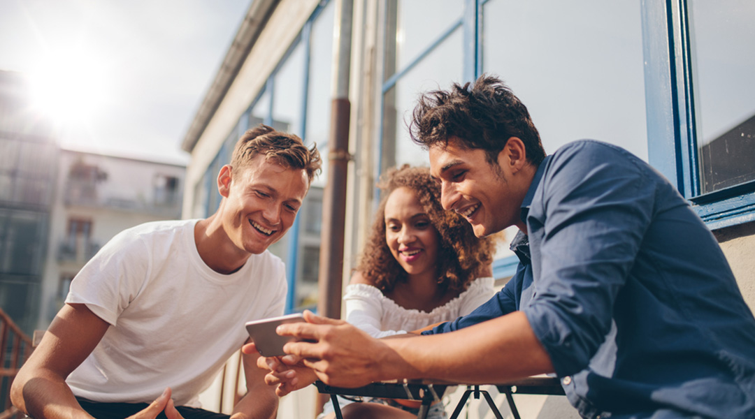 Two men and a woman smiling and looking down at a phone together